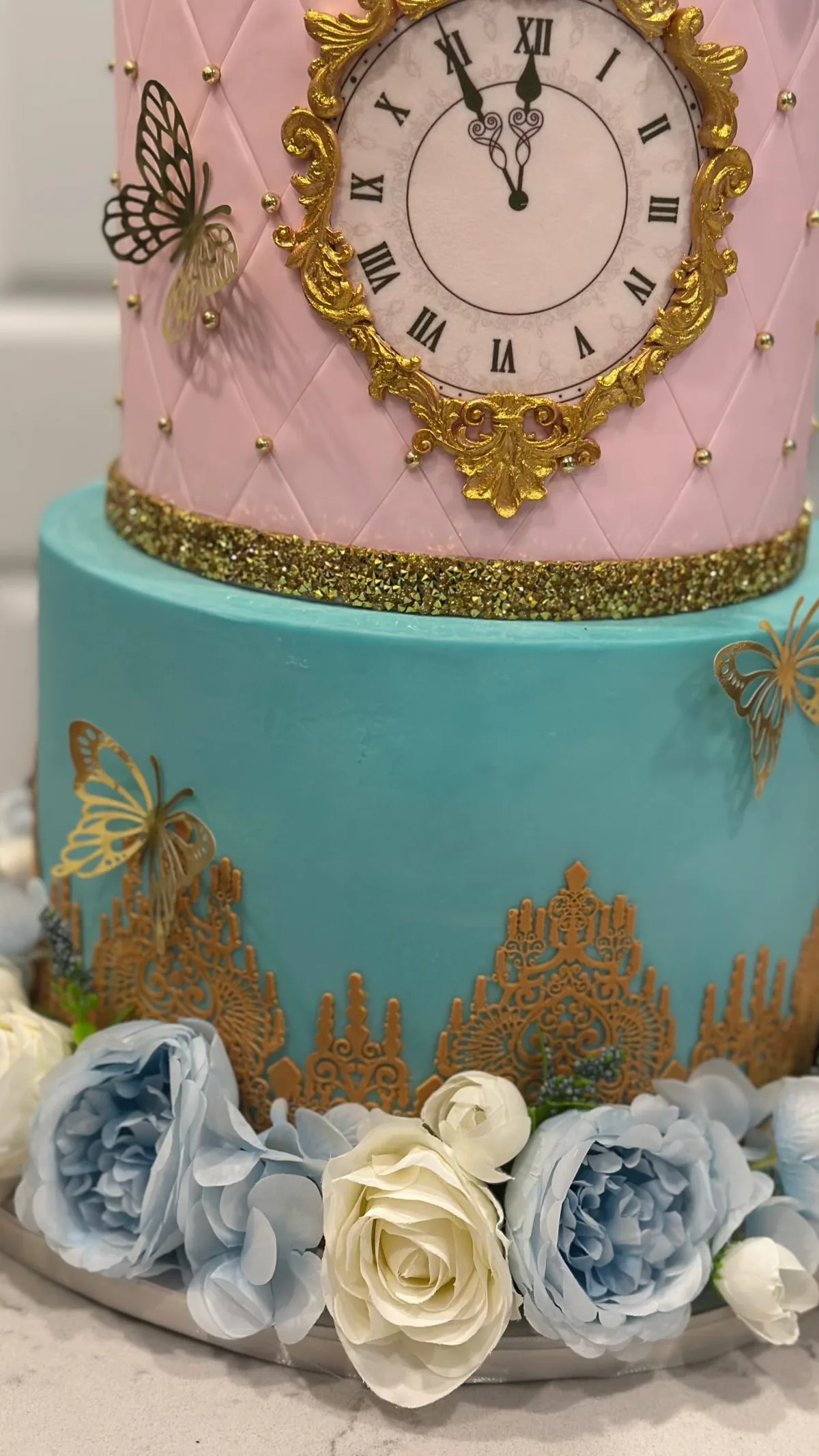 Two tier pink and teal cake with a gold clock and blue roses